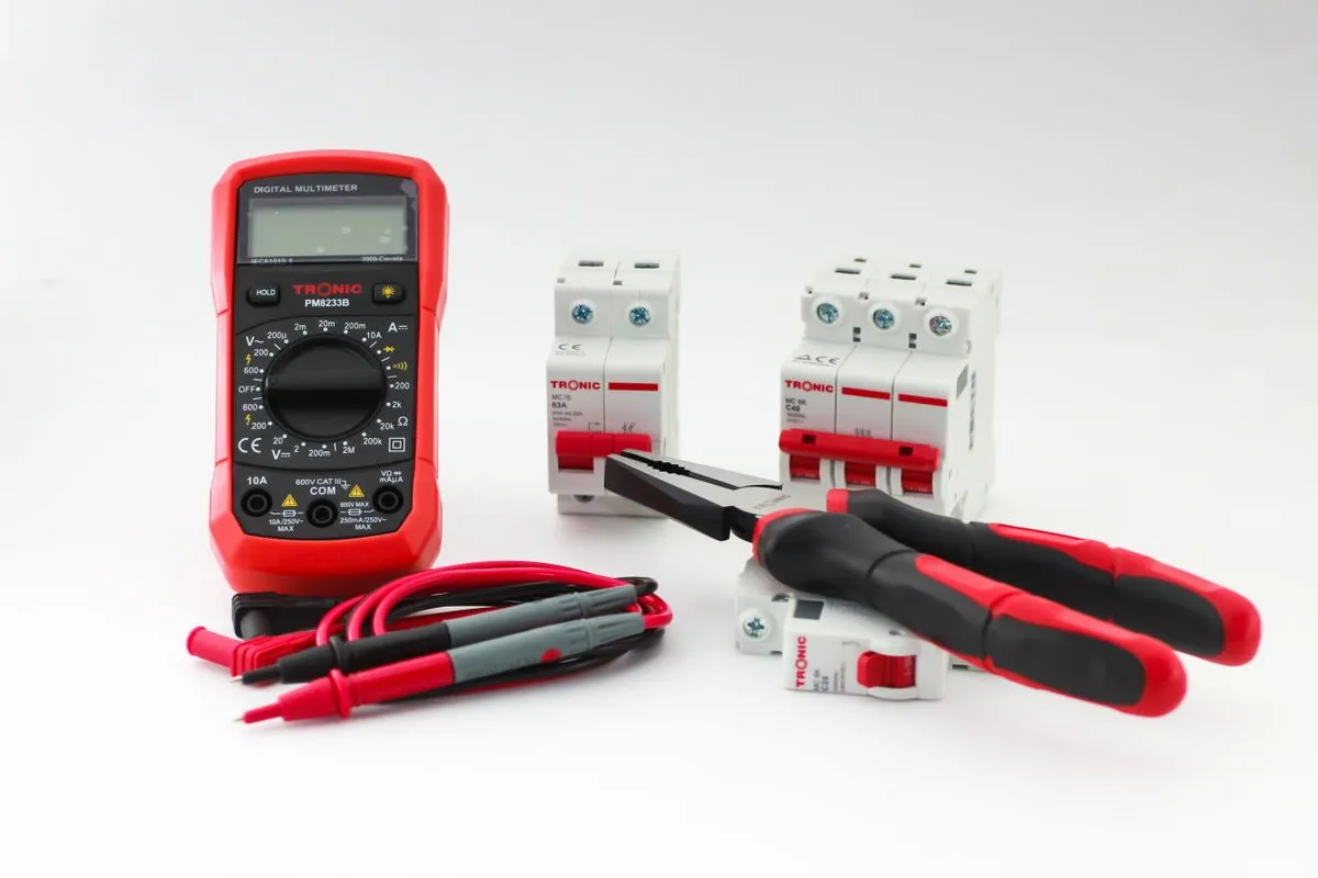 Multimètre numérique et outils d'électricien posés à côté d'un tableau électrique