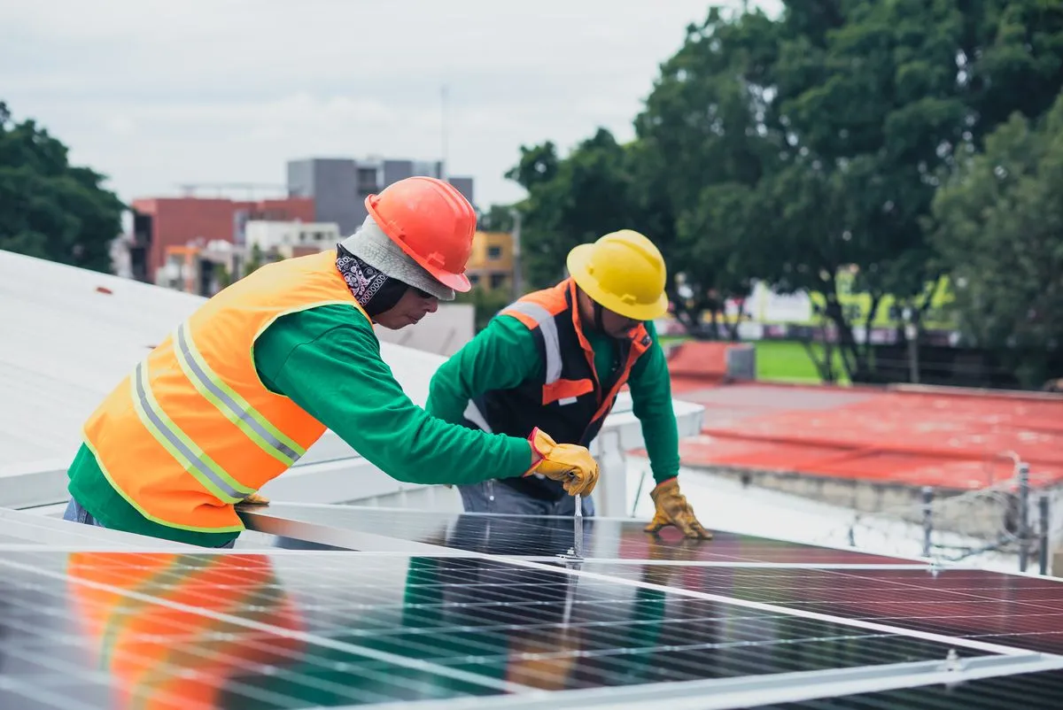 Deux installateurs équipés de harnais posant des panneaux solaires sur un toit